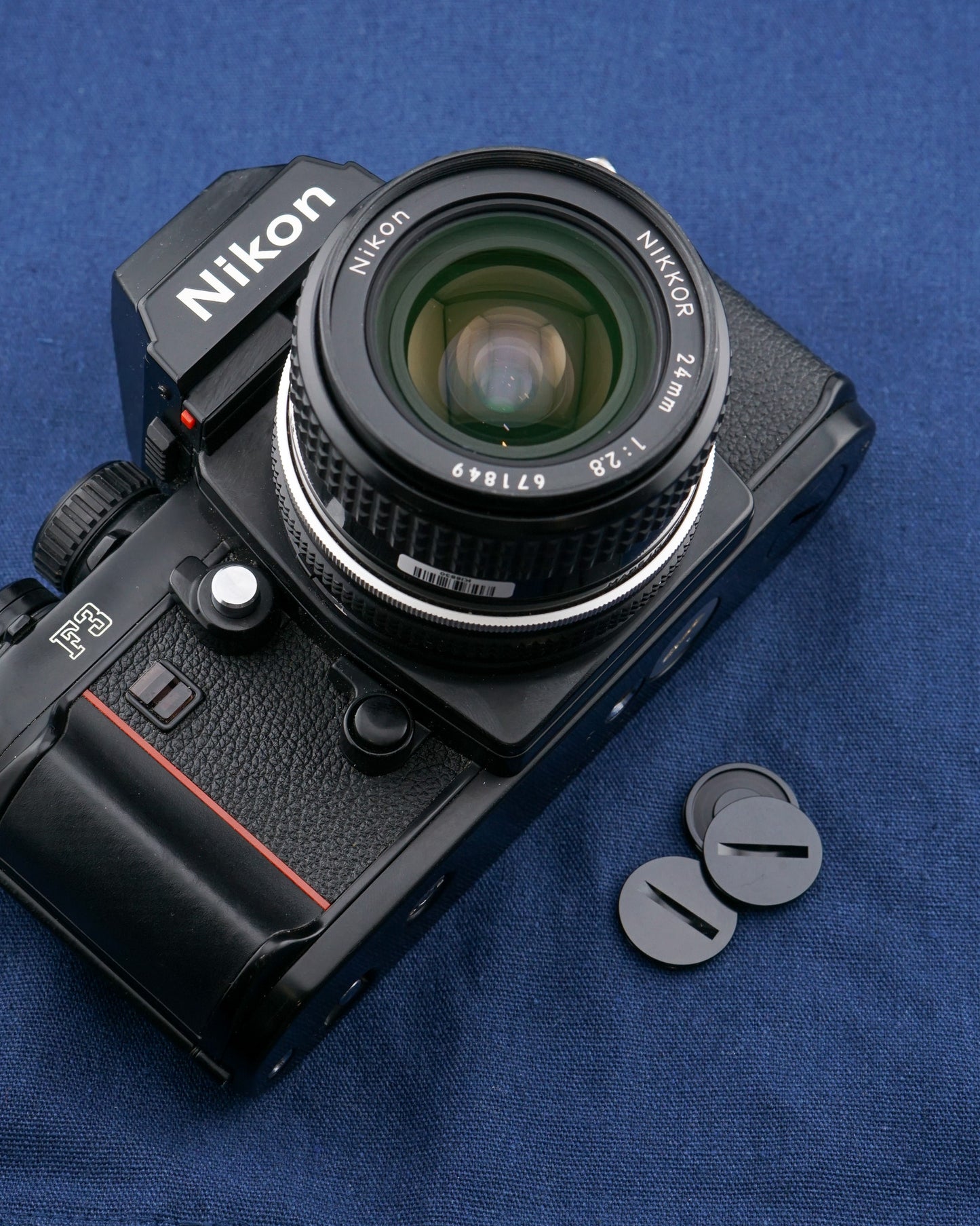 An aftermarket motor drive coupling cover besides a camera body on a blue background. For Nikon bodies.