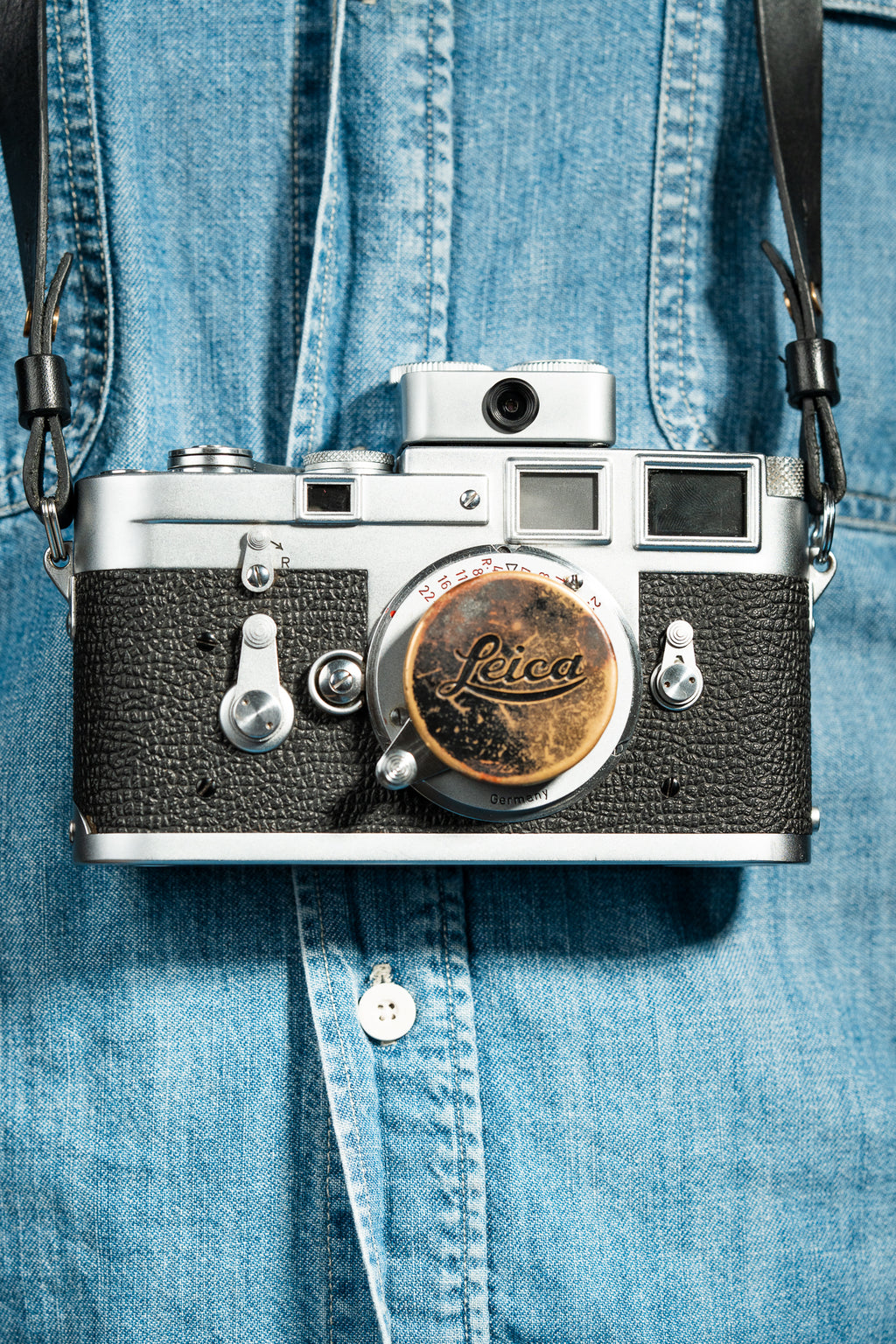 A front-side shot of a camera strapped on a person. A chrome Doomo Meter D hot shoe light meter attached to top of a camera.