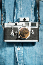 A front-side shot of a camera strapped on a person. A chrome Doomo Meter D hot shoe light meter attached to top of a camera.