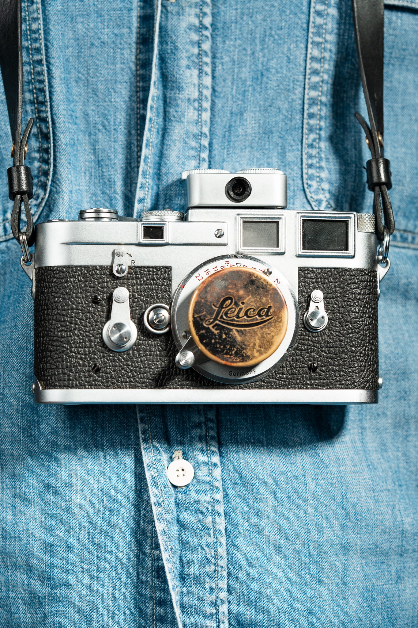 A front-side shot of a camera strapped on a person. A chrome Doomo Meter D hot shoe light meter attached to top of a camera.