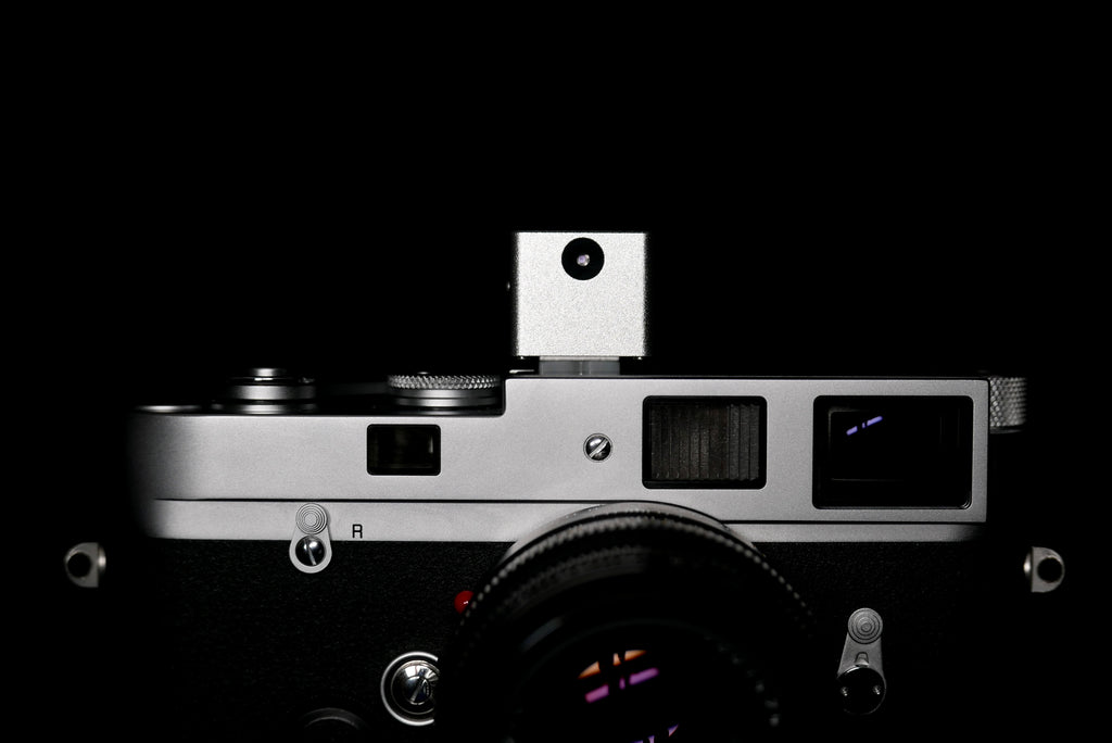 A frontal close-up of KMQ chrome model attached to a camera on a black background.