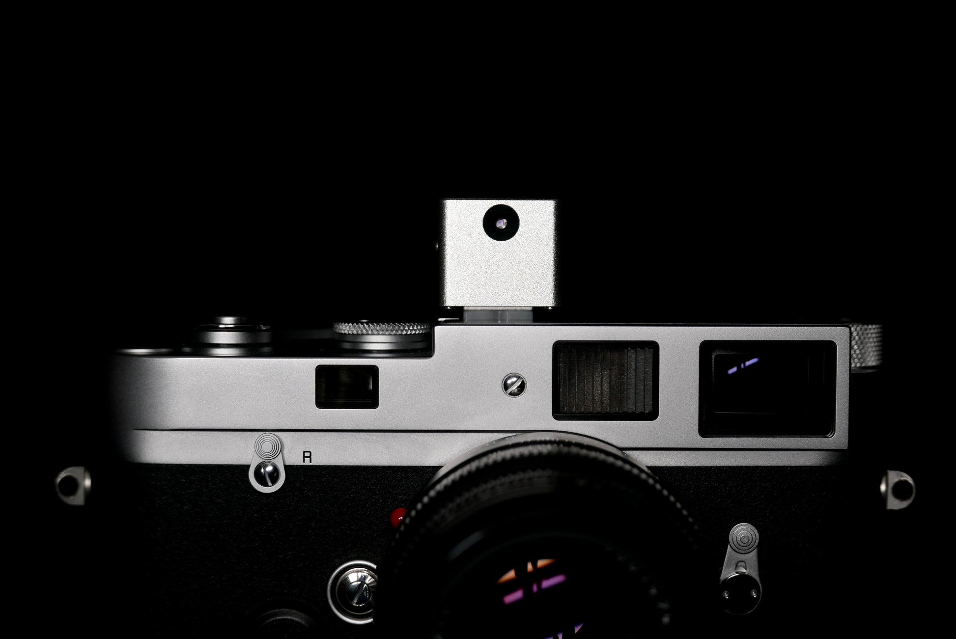 A frontal close-up of KMQ chrome model attached to a camera on a black background.