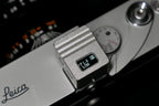 A close-up of KMQ chrome top display model attached to a camera on a black background.