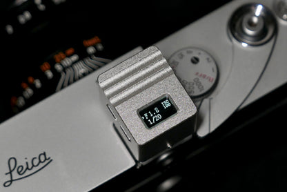 A close-up of KMQ chrome top display model attached to a camera on a black background.