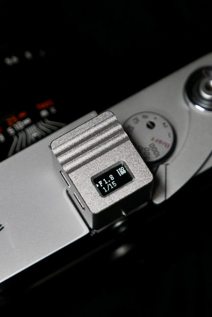 A close-up of KMQ chrome top display model attached to a camera on a black background.