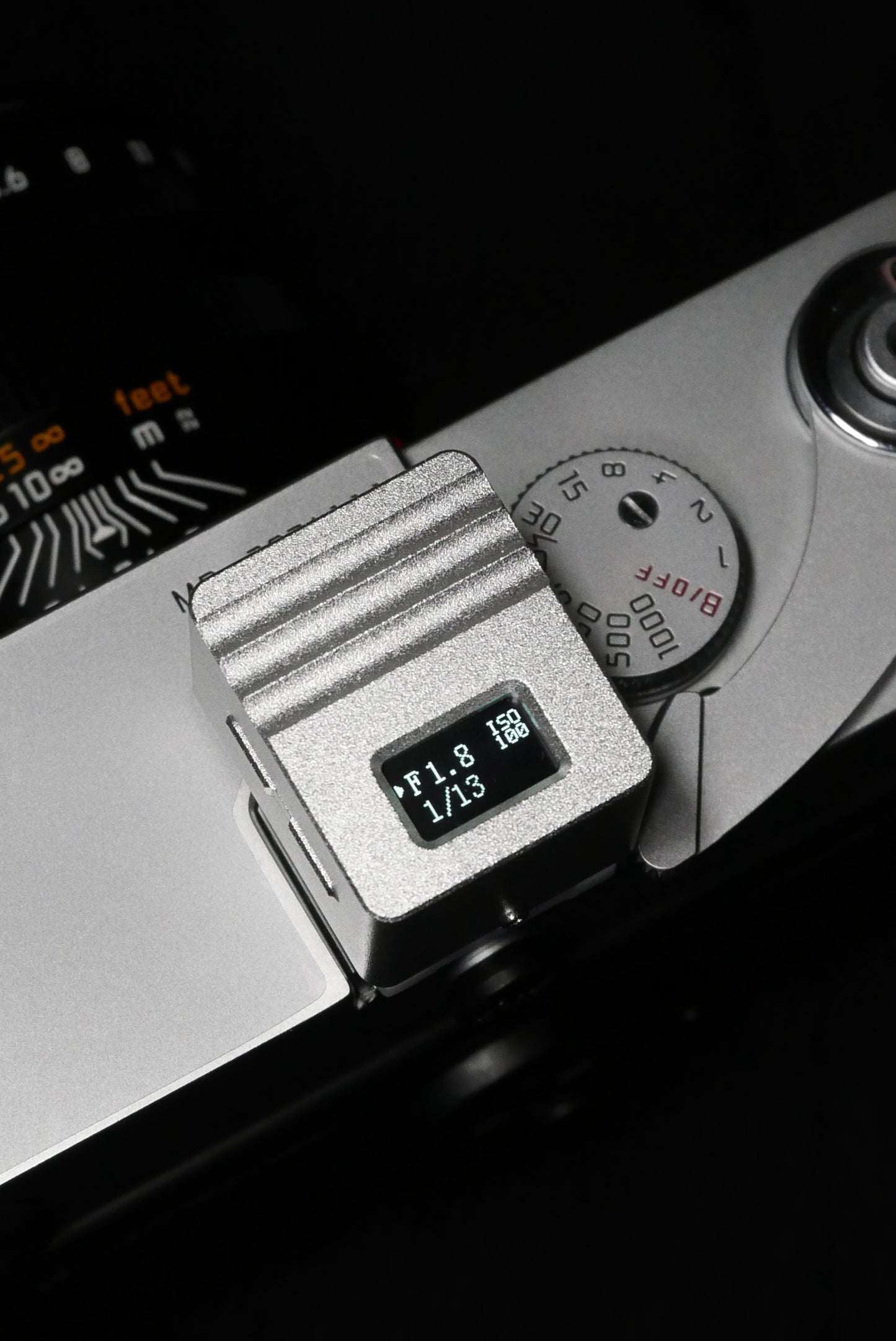 A close-up of KMQ chrome top display model attached to a camera on a black background.