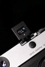 A close-up of KMQ black back display model attached to a camera on a black background.