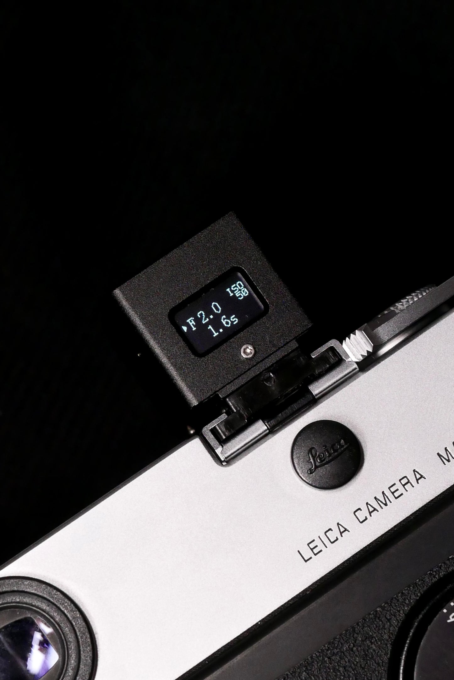 A close-up of KMQ black back display model attached to a camera on a black background.