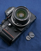 An aftermarket motor drive coupling cover besides a camera body on a blue background. For Nikon bodies.