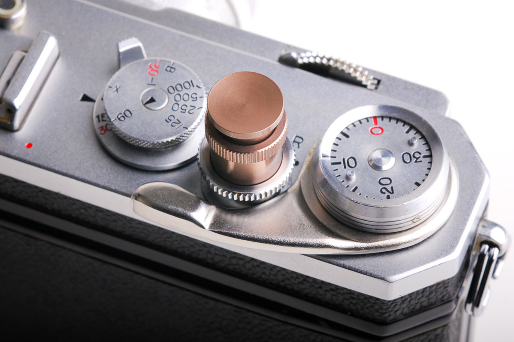 A bronze soft release button attached to a camera on a white background. For Nikon AR-1.