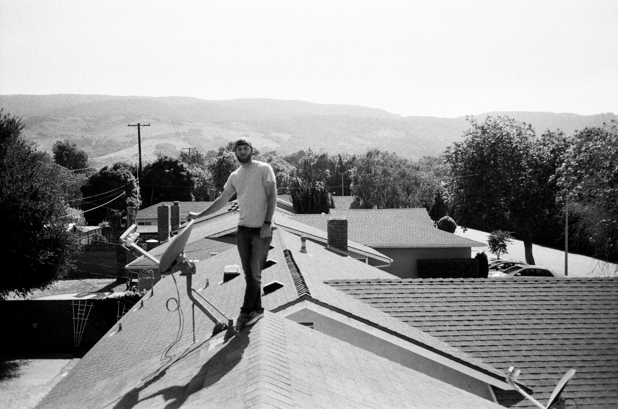 A black and white photo of a man standing on top of a house. 