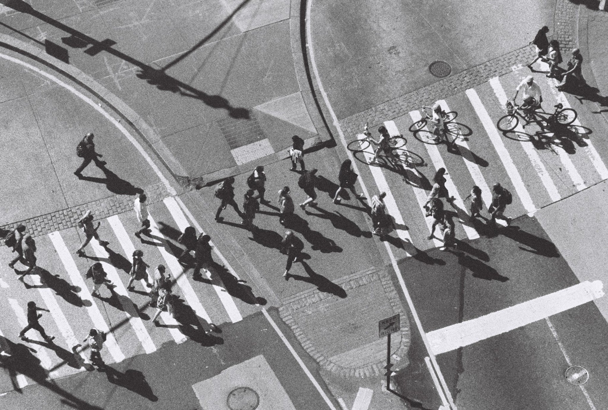 An aerial black and white photo of fast moving pedestrians crossing the street. 