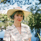 A woman with a hat and some trees and lake on the background. 