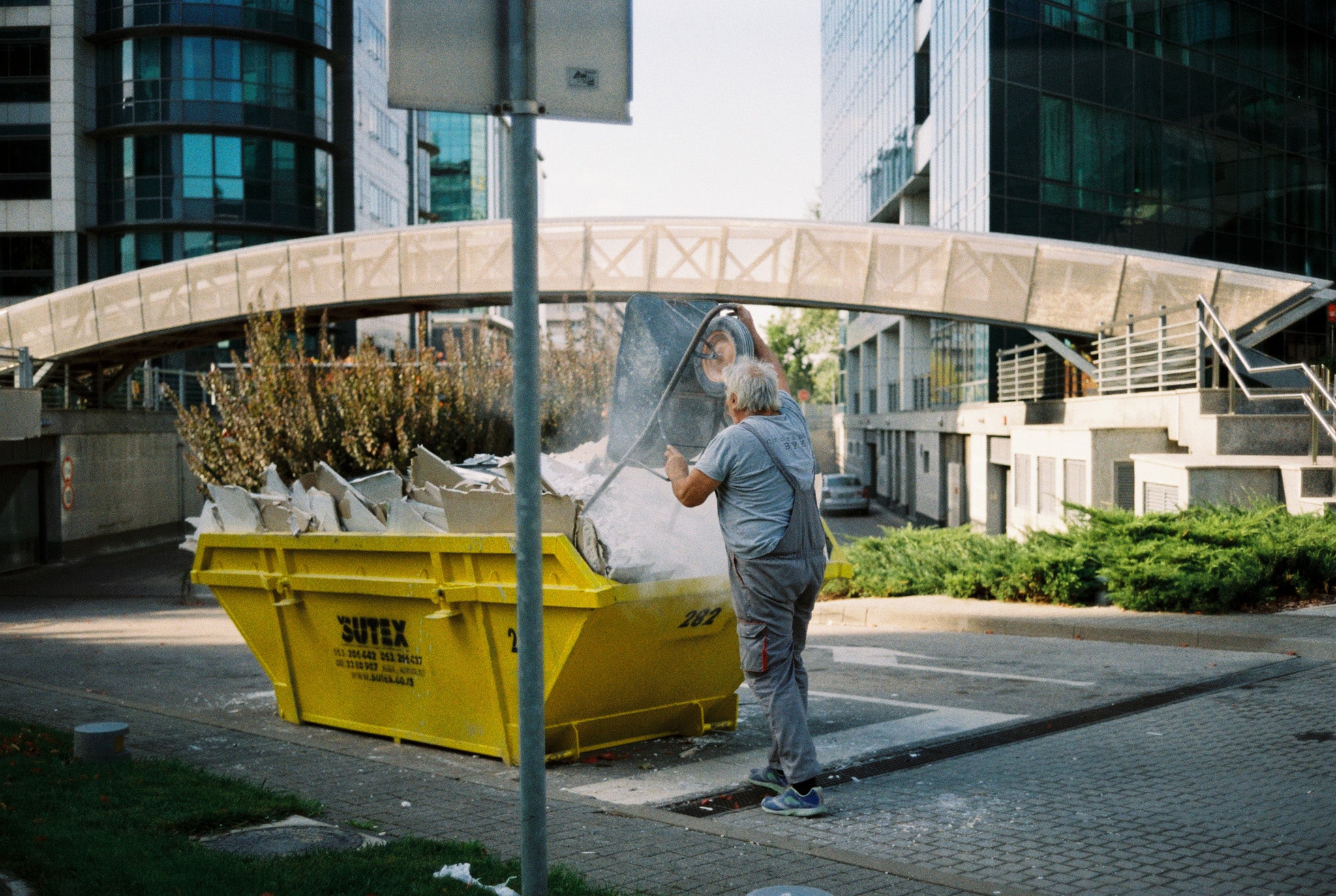A worker emptying trash to a container with city buildings on the background.