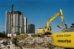 Construction area and excavators in the foreground with some buildings and clear blue sky on the background.