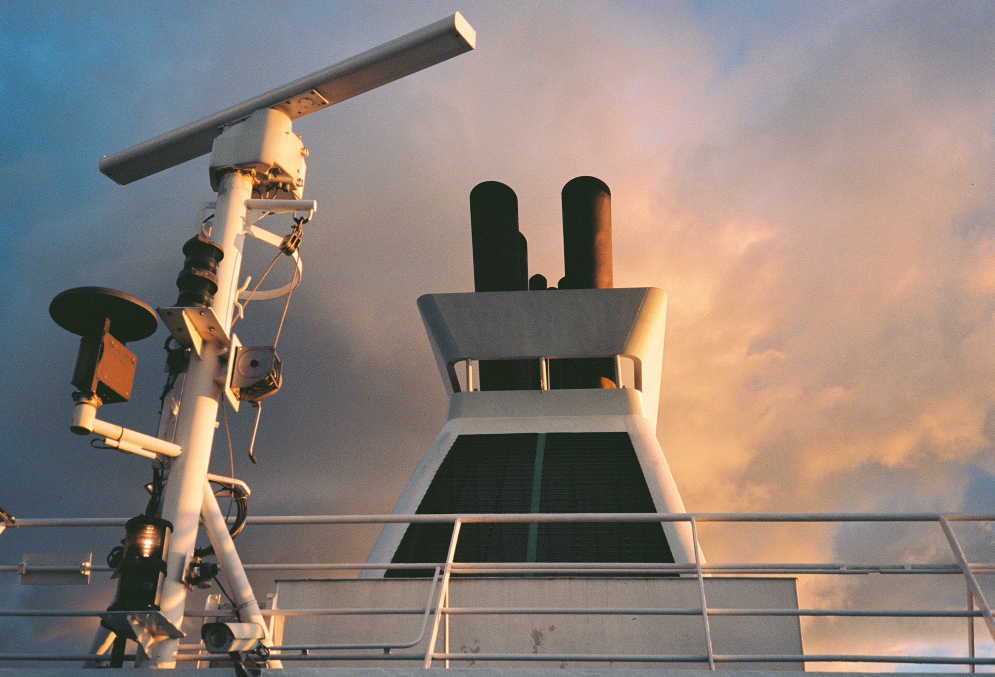 A ship's deck with equipment and ship's helm in the foreground and cloudy sky on the background.