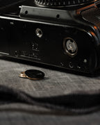 A brass aftermarket motor drive coupler / cover cap on a table in front of a camera body. For Canon EOS-1 film bodies.